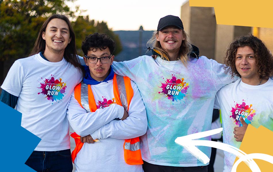 Four students wearing matching Glow Run event shirts standing together outdoors, posing for a group photo during a campus community event.