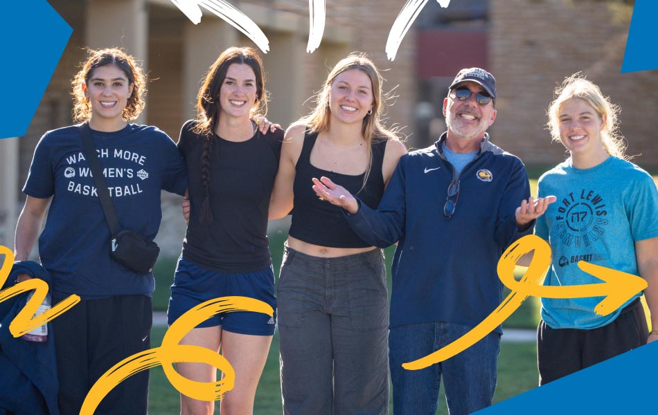 Faculty member standing with four students outdoors on campus, smiling together in an informal group photo on an athletic field.