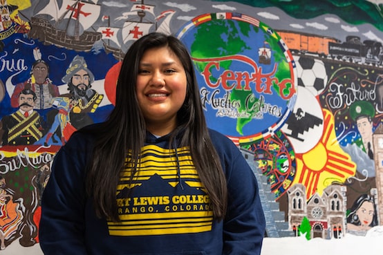 student in FLC sweatshirt stands in front of a mural at Centro de muchos colores