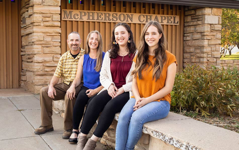 Group of four people seated outdoors in front of McPherson Chapel on the Fort Lewis College campus, with the chapel entrance and stone architecture visible in the background