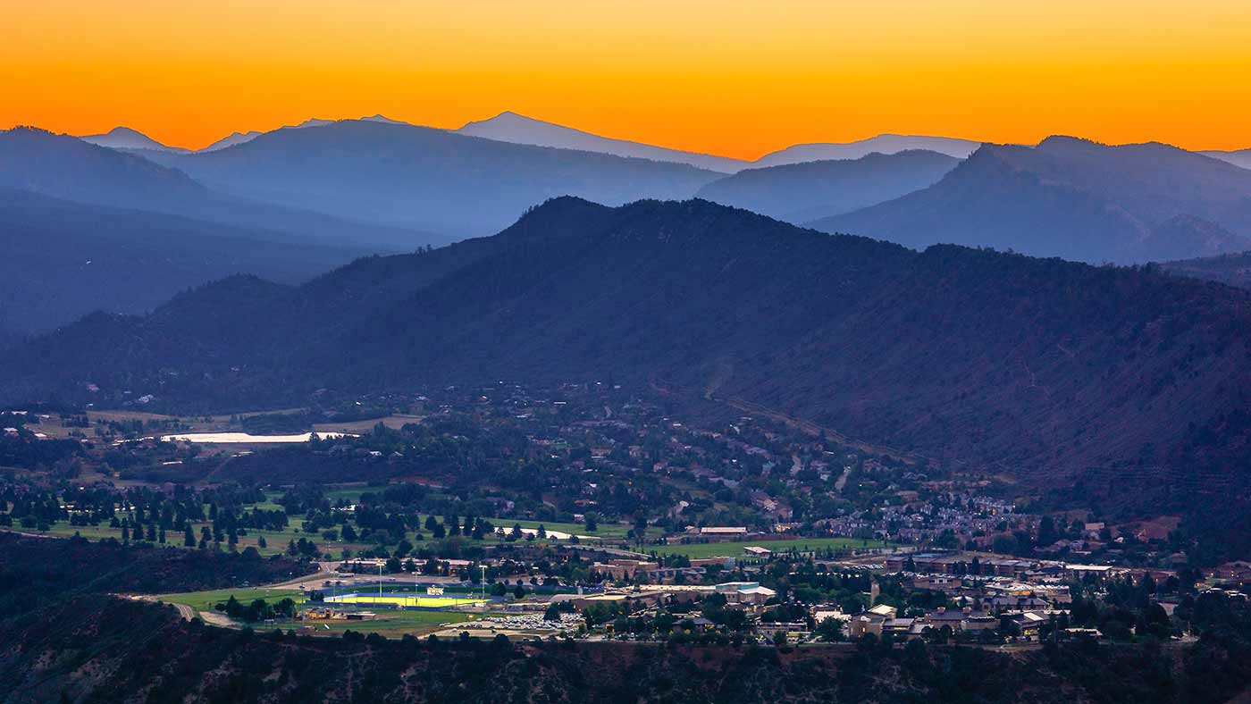 Panoramic view of Durango, Colorado at sunset, with the town below and layered mountain ridgelines extending into the distance.