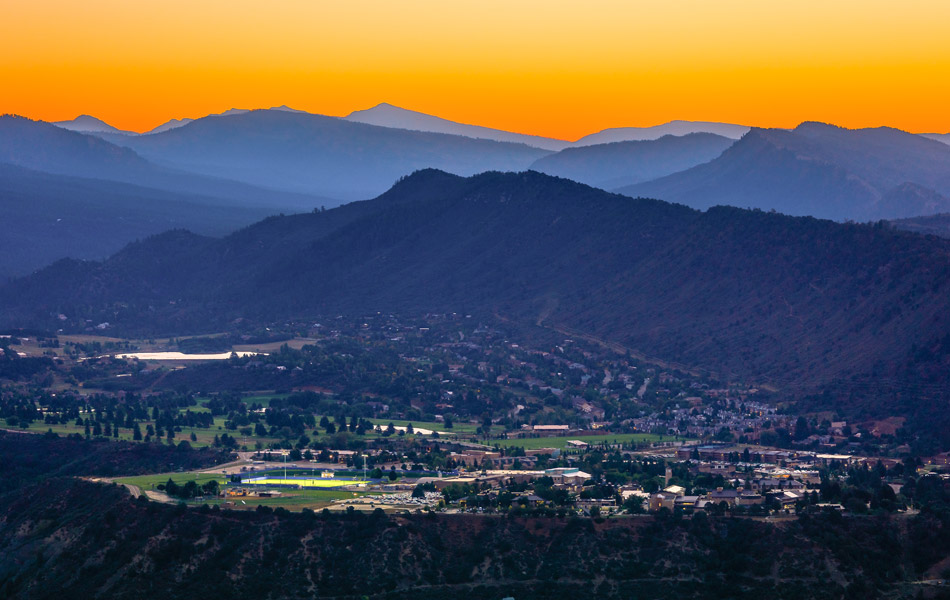 Panoramic view of Durango, Colorado at sunset, with the town nestled in a valley surrounded by layered mountain ridges.