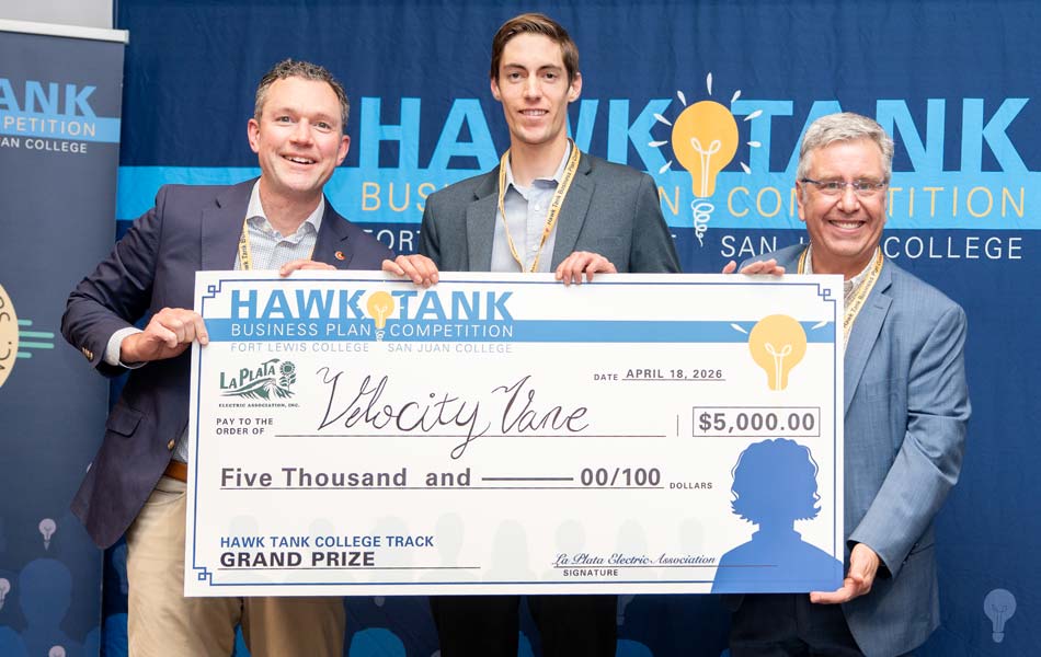 Three individuals standing together holding a large ceremonial check at a Hawk Tank business plan competition, with event branding displayed behind them.